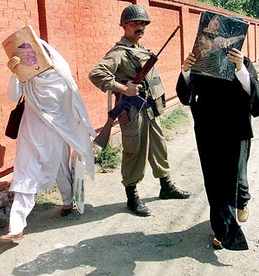 College girls hide their faces with their text books while a trooper keeps guard in Srinagar