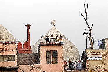 Muslim children sit on the roof of a house next to a mosque