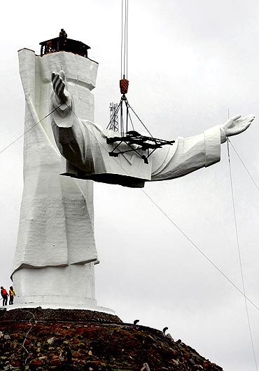A crane lifts the arms of the statue to be pieced together with his body