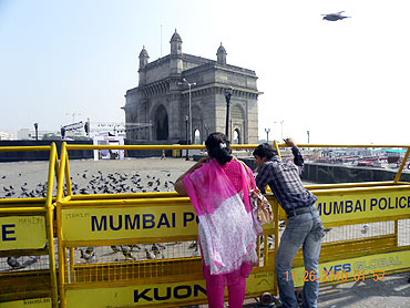 Visitors observe the Gateway of India behind security barricades, adjacent to the Taj Mahal Hotel, at Colaba on Friday