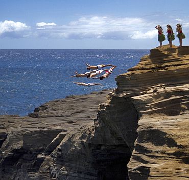 Orlando Duque and Eber Pava of Colombia, Gary Hunt of England, Hassan Mouti of France and Kent De Mond of the US dive from a 16 metre (53 feet) rock at Lana'i Lookout as some local hula girls look on in the lead up to the final round of the 2010 Red Bull Cliff Diving World Series in Oahu, Hawaii, on September 8