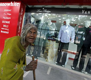 file photo shows a beggar walking past a shop window with designer clothes in New Delhi