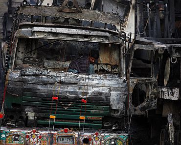 A man searches through a damaged truck, carrying supplies to foreign forces in Afghanistan, after it was attacked and burnt in a field in Sangjani, located in the outskirts of Islamabad