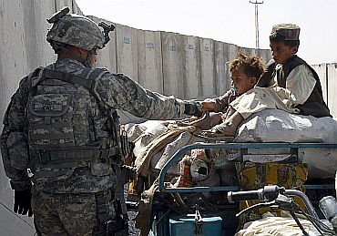 A US soldier greets children while their father is being checked at a joint military checkpoint in Kandahar