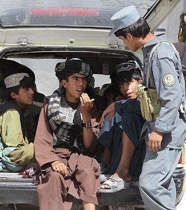 An Afghan policeman interrogates passengers of a vehicle at a joint military checkpoint near Kandahar