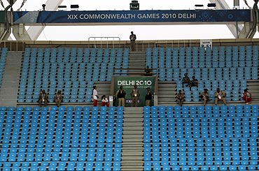 Security and volunteers sit in some empty seats at the Jawaharlal Nehru Stadium