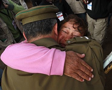 A relative of the 33 miners trapped deep underground in a copper and gold mine is hugged by a policeman after the T 130 drilling machine completed an escape hole for the 33 miners