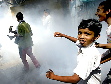 Children play as a health worker fumigates a slum to prevent malaria in Mumbai