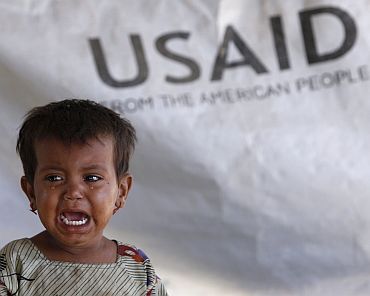 Three-year-old Phaphol cries as she sits in her family's tent, with a weather sheet donated by USAID, while taking refuge on an embankment at Chandan Mori village in Dadu in Pakistan's Sindh province