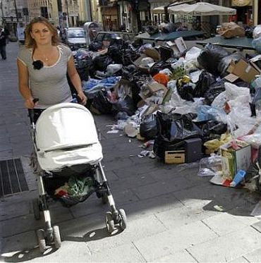 A woman pushes a stroller near a pile of garbage in downtown Naples