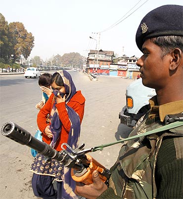 Kashmiri women hide their faces as a policeman stands guard during a curfew in Srinagar