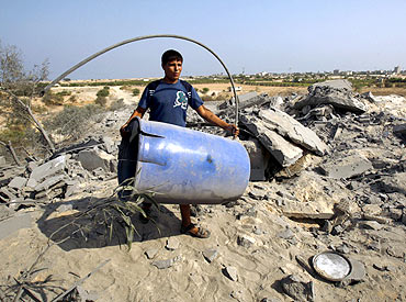 A Palestinian carries a barrel at an abandoned house that was destroyed in an Israeli air strike in Deir al-Balah