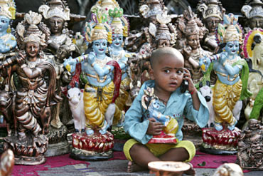 A boy plays with a mobile phone in front of idols of Lord Krishna