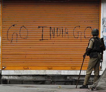 A policeman stands guard in front a closed shop marked with graffiti during a curfew