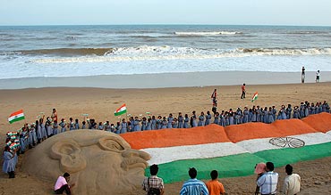 School children gather around a sand sculpture of the Indian national flag and Mahatma Gandhi