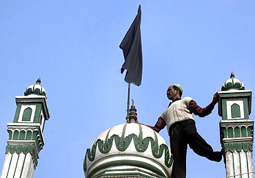 A man hoists a black flag atop a mosque in Ayodhya to observe the anniversary of the Babri Masjid demolition