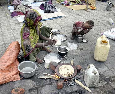 A homeless woman prepares roti on a footpath as a child looks on