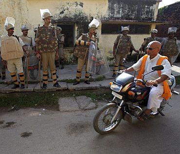 A priest rides a motorcycle as policemen stand guard on a street in Ayodhya