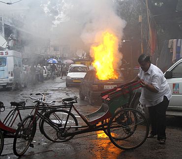 A man removes rickshaws near the car which burst into flames near the scene