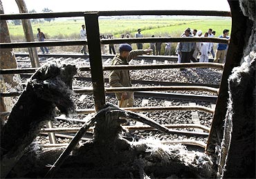 Onlookers stand near the burnt carriage of the Samjhauta Express train after the blast