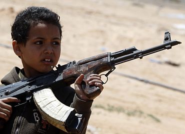 A rebel fighter's son holds a weapon near the front line along the western entrance gate of Ajdabiyah