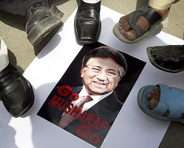 Protestors stand over a poster of Pakistan's President Pervez Musharraf