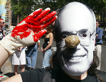 A protester salutes with fake blood on her hands as she wears a mask of Australian Prime Minister John Howard in Sydney
