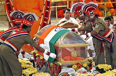 Police personnel place a national tricolour on a glass box containing Sai Baba's body as a mark of respect during his funeral