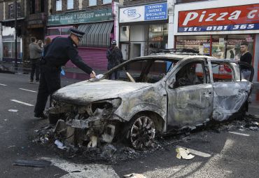 A police officer removes identification from a police car set alight and burned during riots in Tottenham, north London.