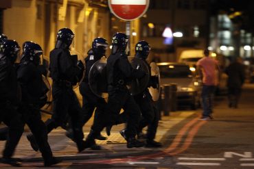 Police officers wearing riot gear run along a street in Tottenham, north London