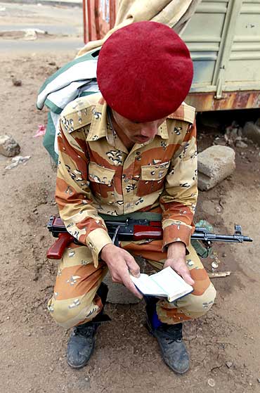 A defected soldier who has joined sides with anti-regime protesters to demand the ouster of Yemen's President Ali Abdullah Saleh, reads a Koran at a checkpoint in Taghyeer (Change) Square in Sanaa