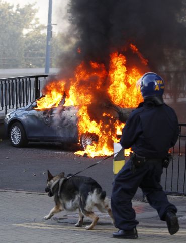 A policeman and his dog walk towards a burning car in central Birmingham, central England
