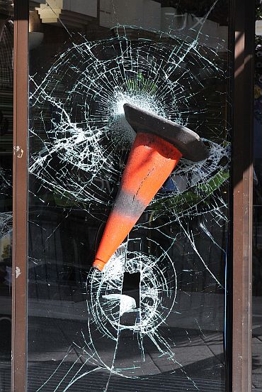A traffic cone is embedded in the smashed windows of a shop
