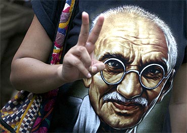 A supporter of Hazare flashes a victory sign while wearing a T-shirt with a photo of Mahatma Gandhi