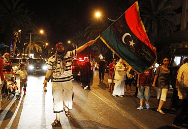 A member of the Libyan community in Tunisia holds the Kingdom of Libya flag as others gather outside the Libyan Embassy in Tunis