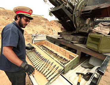 A Libyan rebel fighter prepares anti-aircraft ammunition as he wears the cap of a pro-Muammar Gaddafi officer at Misrata's western front line, some 25 km (16 miles) from the city centre, June 4