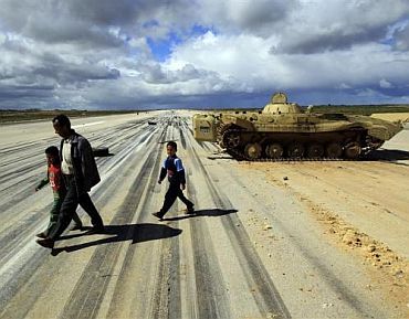 A man walks with his children past an army armoured vehicle at a military airport runway in the eastern Libyan town of Al Abrak February 24