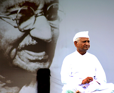 Anna Hazare greets a supporter as he sits in front of a portrait of Mahatma Gandhi, at Ramlila grounds in New Delhi