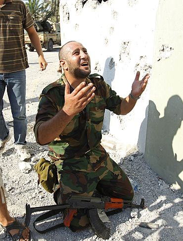 A Libyan rebel fighter prays at the enterance of Bab al-Aziziya compound in Tripoli