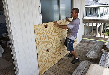 A man positions a sheet of plywood over a sliding glass door as he boards up a house in preparation for Hurricane Irene in Atlantic Beach