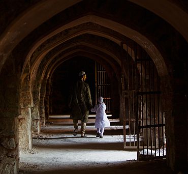 A man and a boy hold hands as they walk through a corridor under the ruins of the Feroz Shah Kotla Mosque in New Delhi after prayers