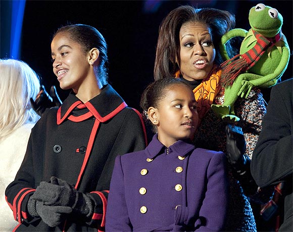 U.S. first lady Michelle Obama sings a Christmas carol with her daughters Malia (L) and Sasha and Kermit the Frog during the lighting of the National Christmas Tree in Washington