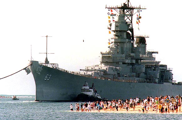 The battleship USS Missouri, Mighty Mo, looms over a gathering of fans as it returns to Pearl Harbor. The USS Missouri, the ship where the Japanese and the United States signed the agreement to end World War II, will be used as a museum near the memorial to the USS Arizona