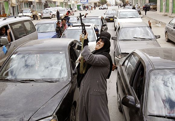 A woman rebel fighter supporter shoots an AK-47 rifle as she reacts to the news of the withdrawal of Libyan leader Muammar Gaddafi's forces from Benghazi March 19