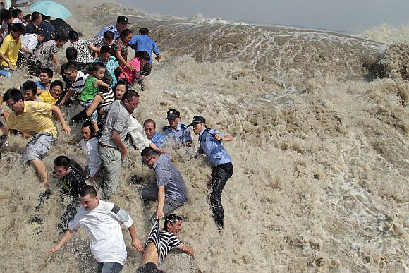 Policemen and residents run as waves from a tidal bore surge past a barrier on the banks of Qiantang River in Haining, Zhejiang province August 31, 2011. As Typhoon Nanmadol approaches eastern China, the tides and waves in Qiantang River recorded its highest level in 10 years