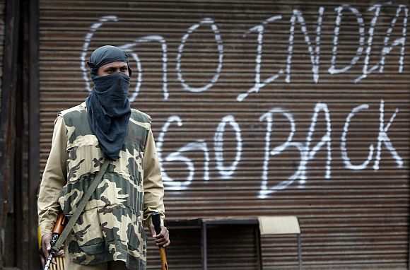 An security personnel stands guard near a closed shop during a curfew in Srinagar