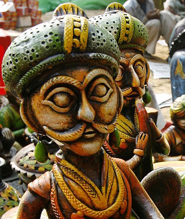 Labourers sit near a stall of sculptures at the Surajkund Crafts Fair