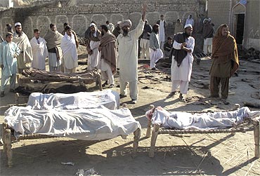 Villagers stand beside bodies of blast victims, near the site of a suicide bomb attack, in the town of Lakki Marwat in Pakistan