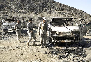Afghan border police keep watch next to burnt vehicles belonging to a team of Afghan deminers who were kiddnapped by the Taliban