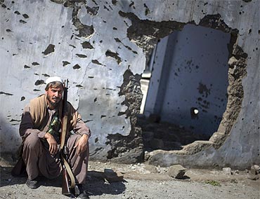 A member of the local Lashkar sits with his weapon next to a wall damaged in recent fighting along the Afghanistan-Pakistan border